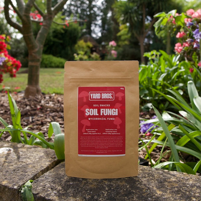 Bag of Yard Buds Soil Fungi product on a stone ledge with a garden background